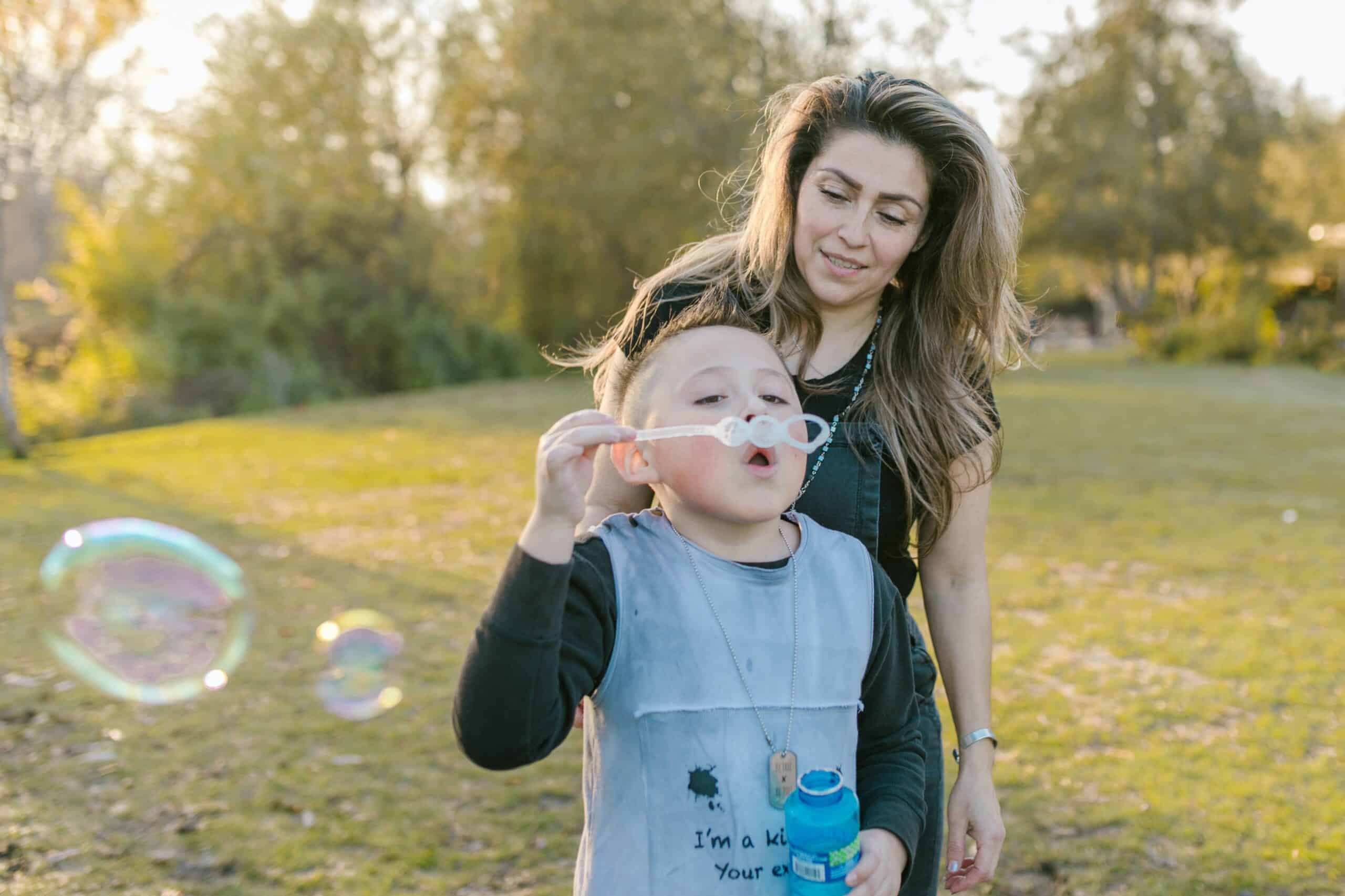 Cheerful nanny and a boy having a delightful time blowing bubbles in a park, showcasing the immediate availability and trustworthy care provided by Lifetime of Love Nannies