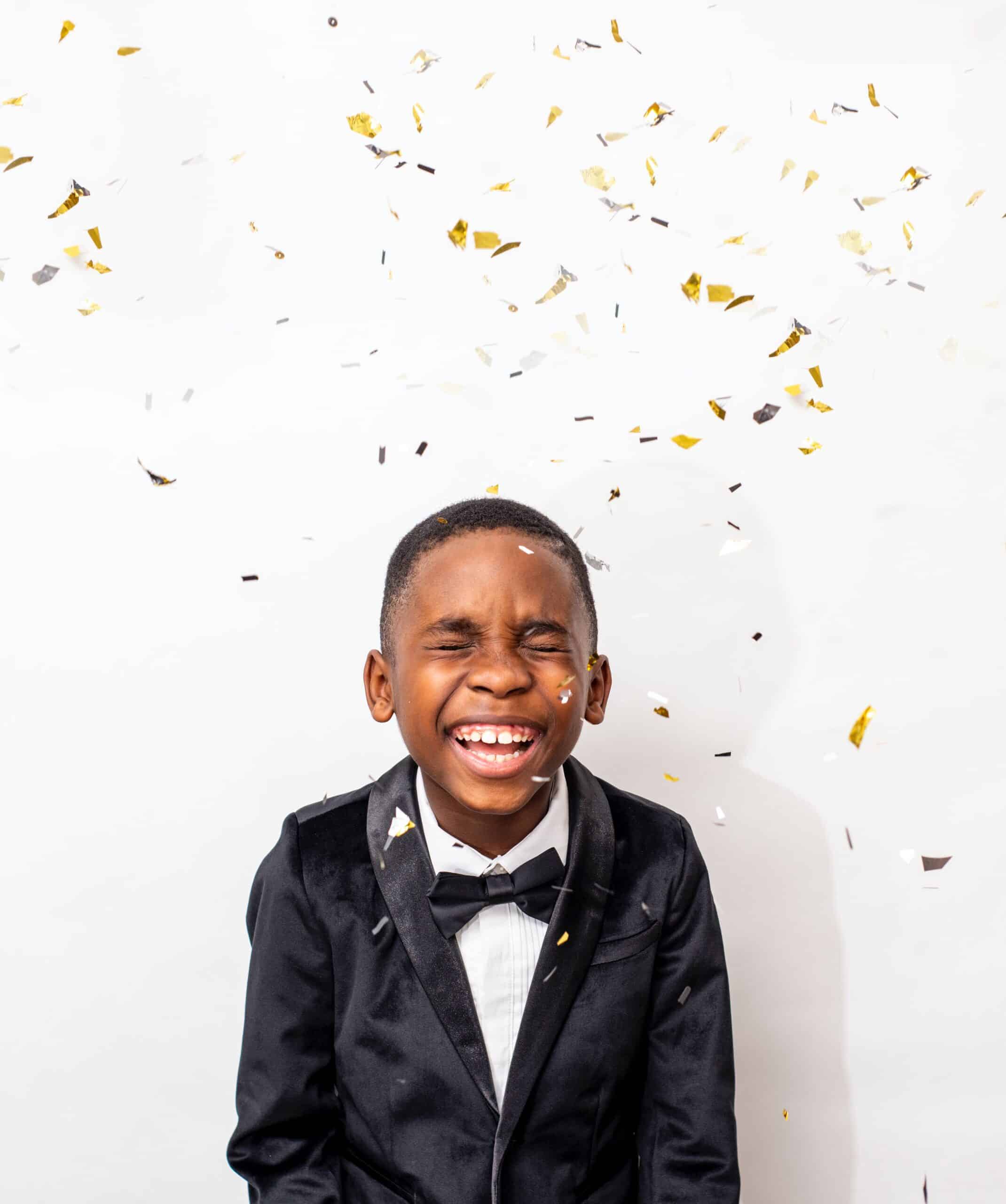 Joyful boy with a big smile closing his eyes as confetti flies around the room highlighting the fun and engaging atmosphere created by Lifetime of Love Nannies scaled