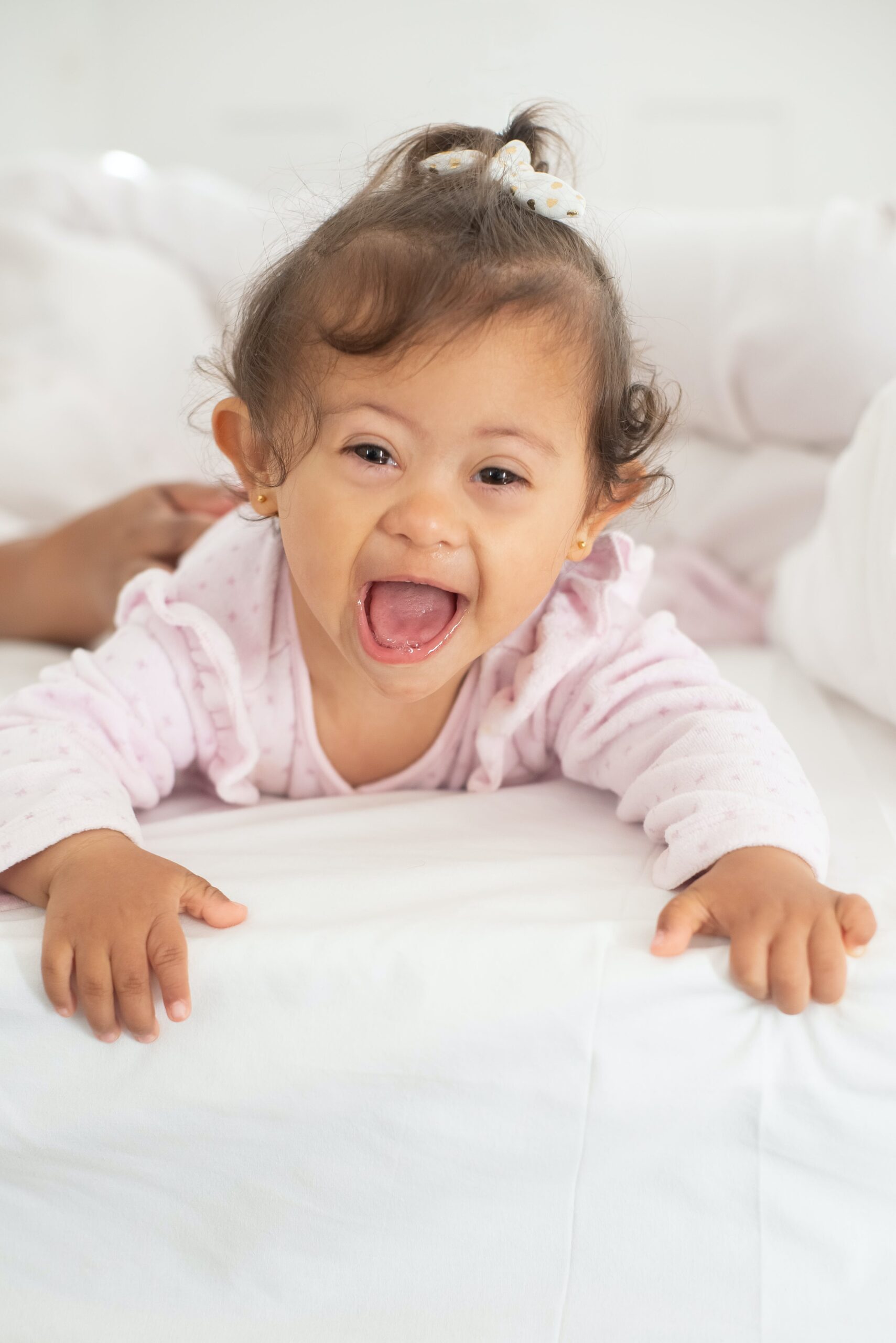 Joyful little girl with special needs actively crawling on a bed, highlighting the personalized, adaptive, and supportive care provided by Lifetime of Love Nannies