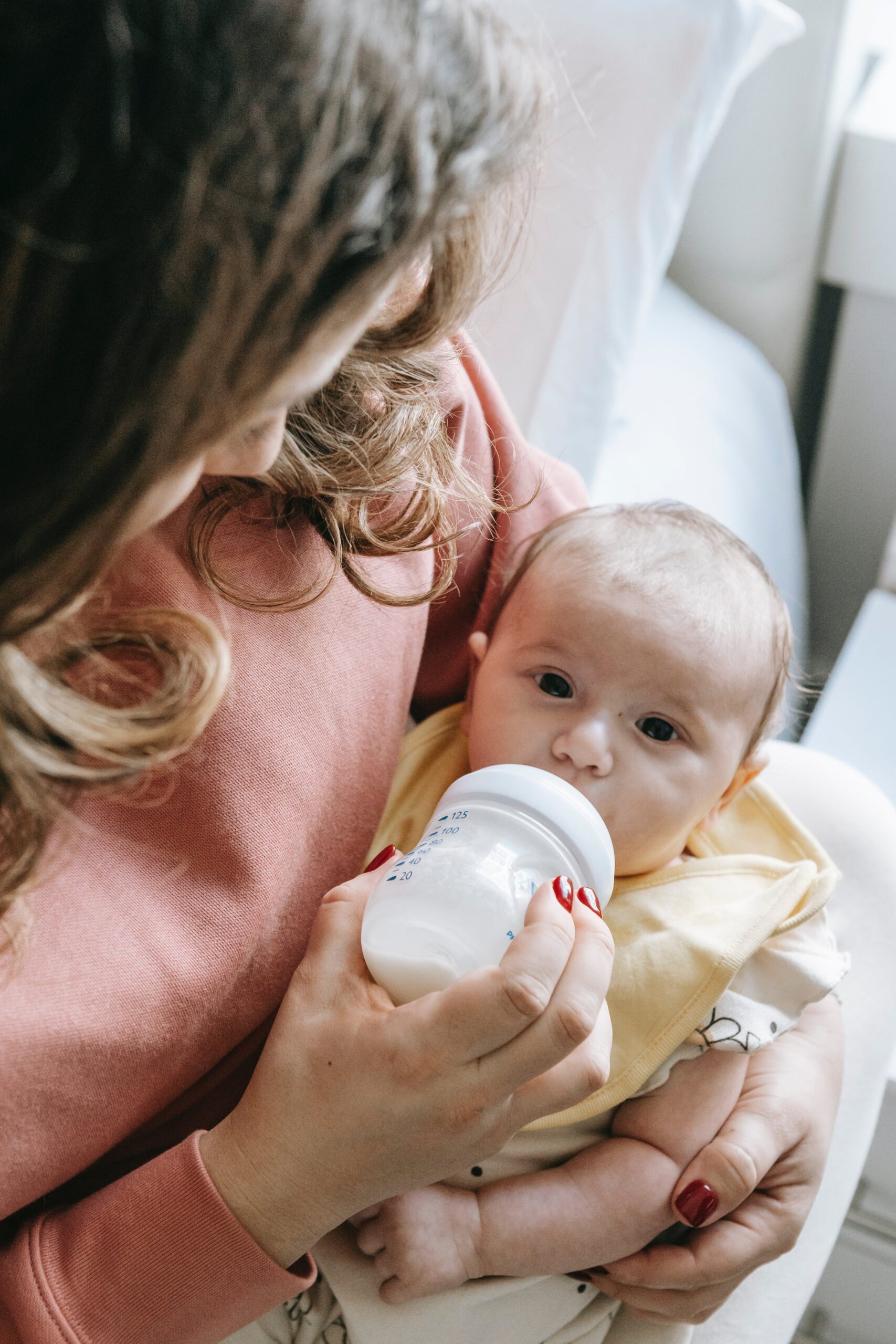 Newborn care specialist attentively giving milk to a baby with a feeding bottle, showcasing the specialized, 24 7 supportive care provided by Lifetime of Love Nannies