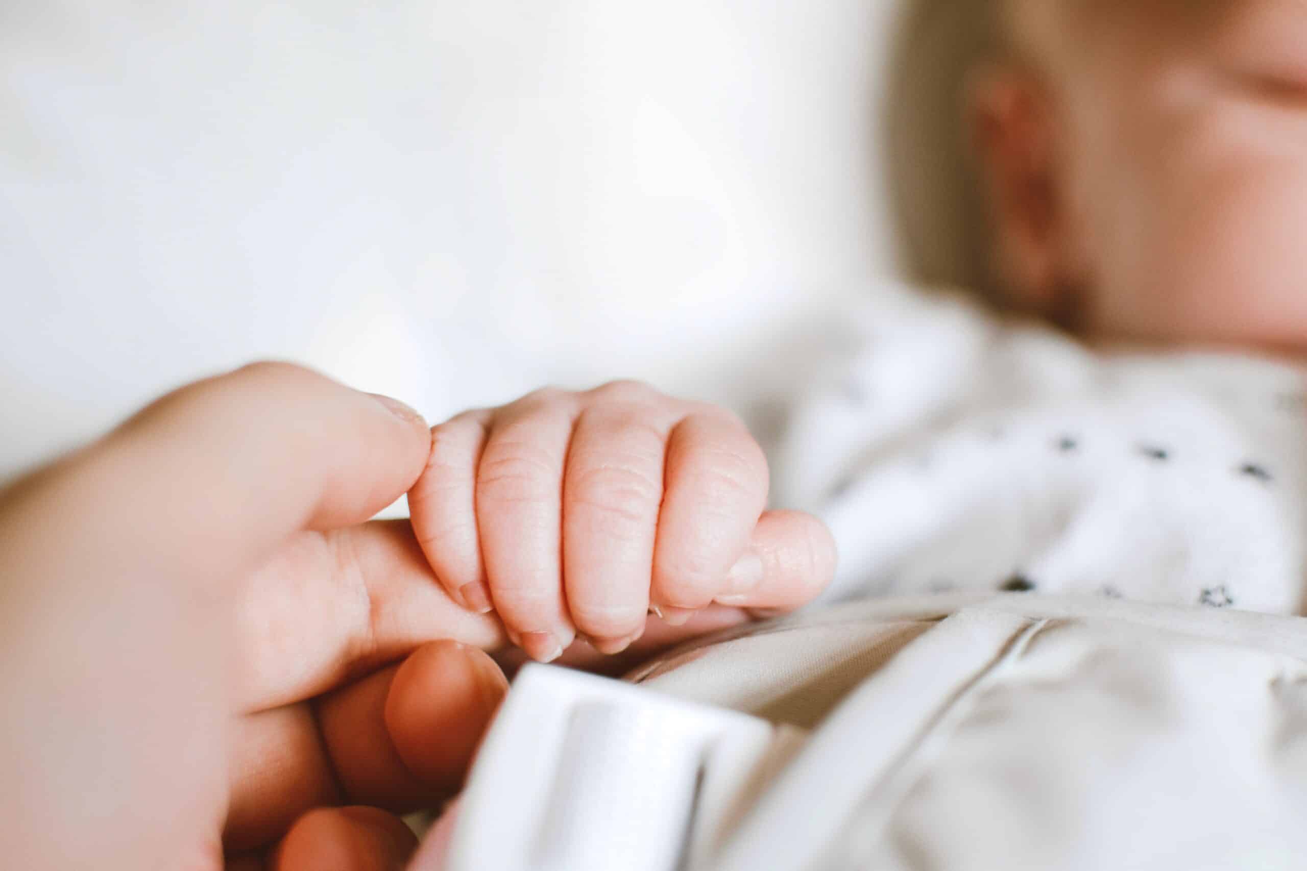 Tiny newborn baby tenderly grabbing an adult's finger, capturing the intimate and supportive newborn and infant care provided by Lifetime of Love Nannies