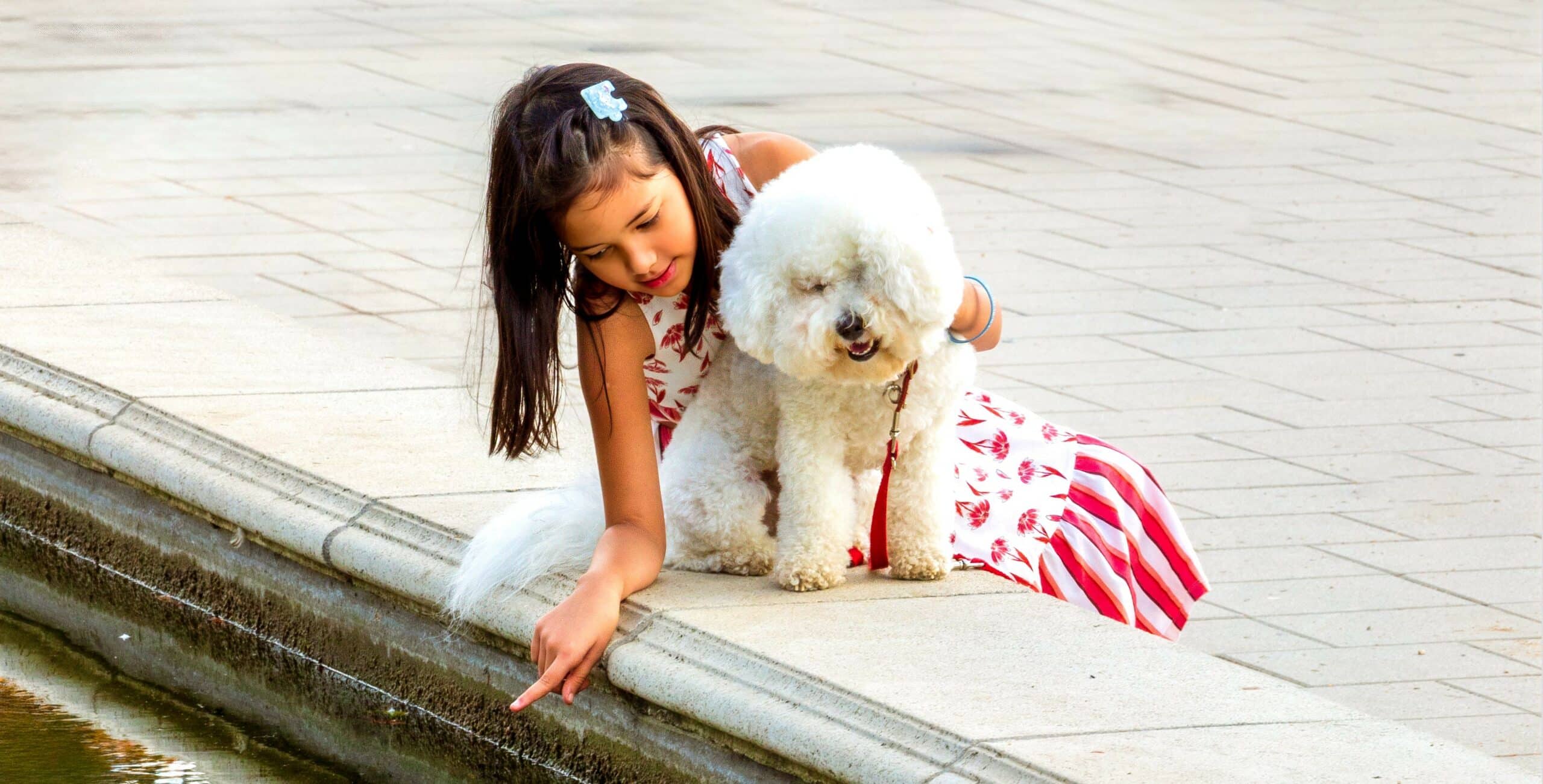 Little girl sitting with her dog by a fountain in a Las Vegas park, enjoying a sunny day safely