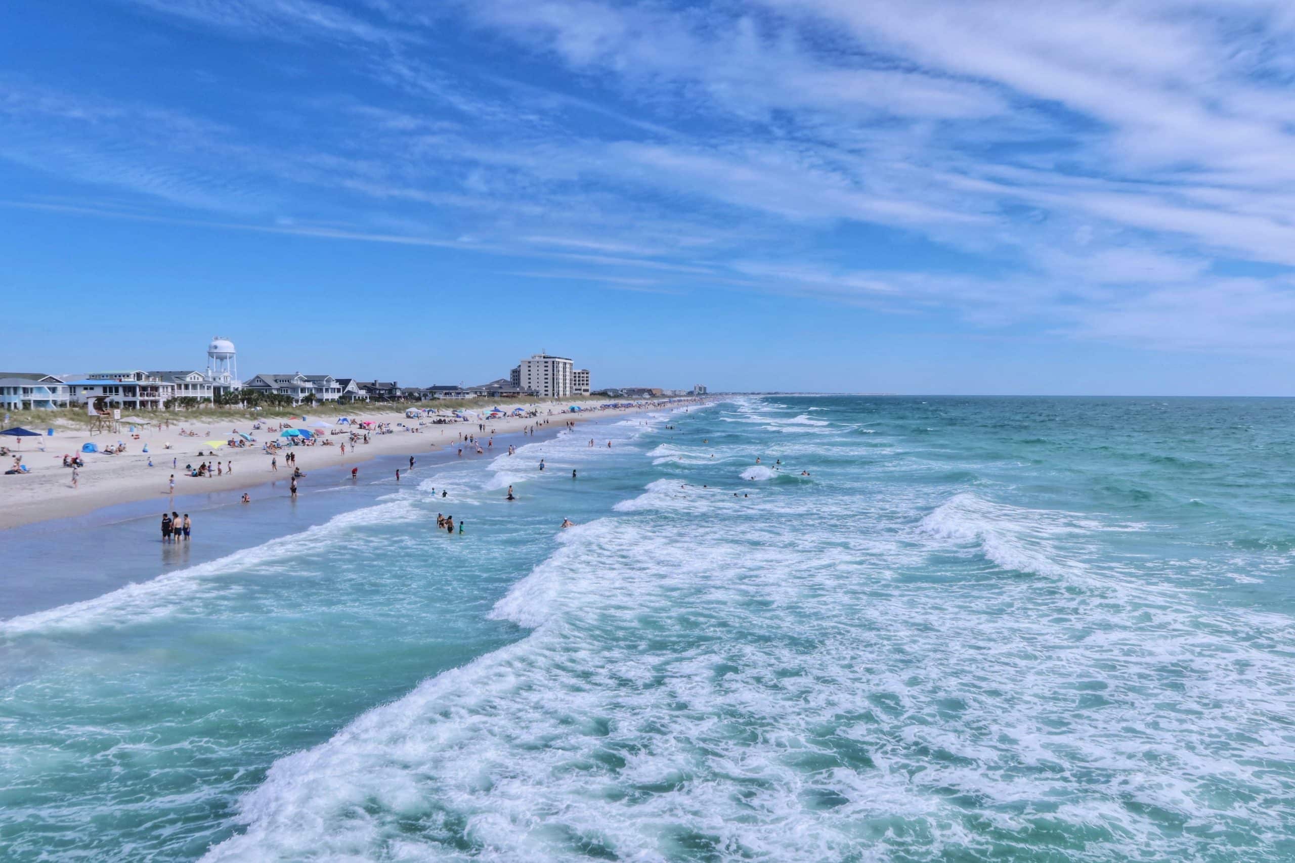 Wrightsville Beach North Carolina coastline with families swimming in turquoise Atlantic Ocean waves on a sunny day