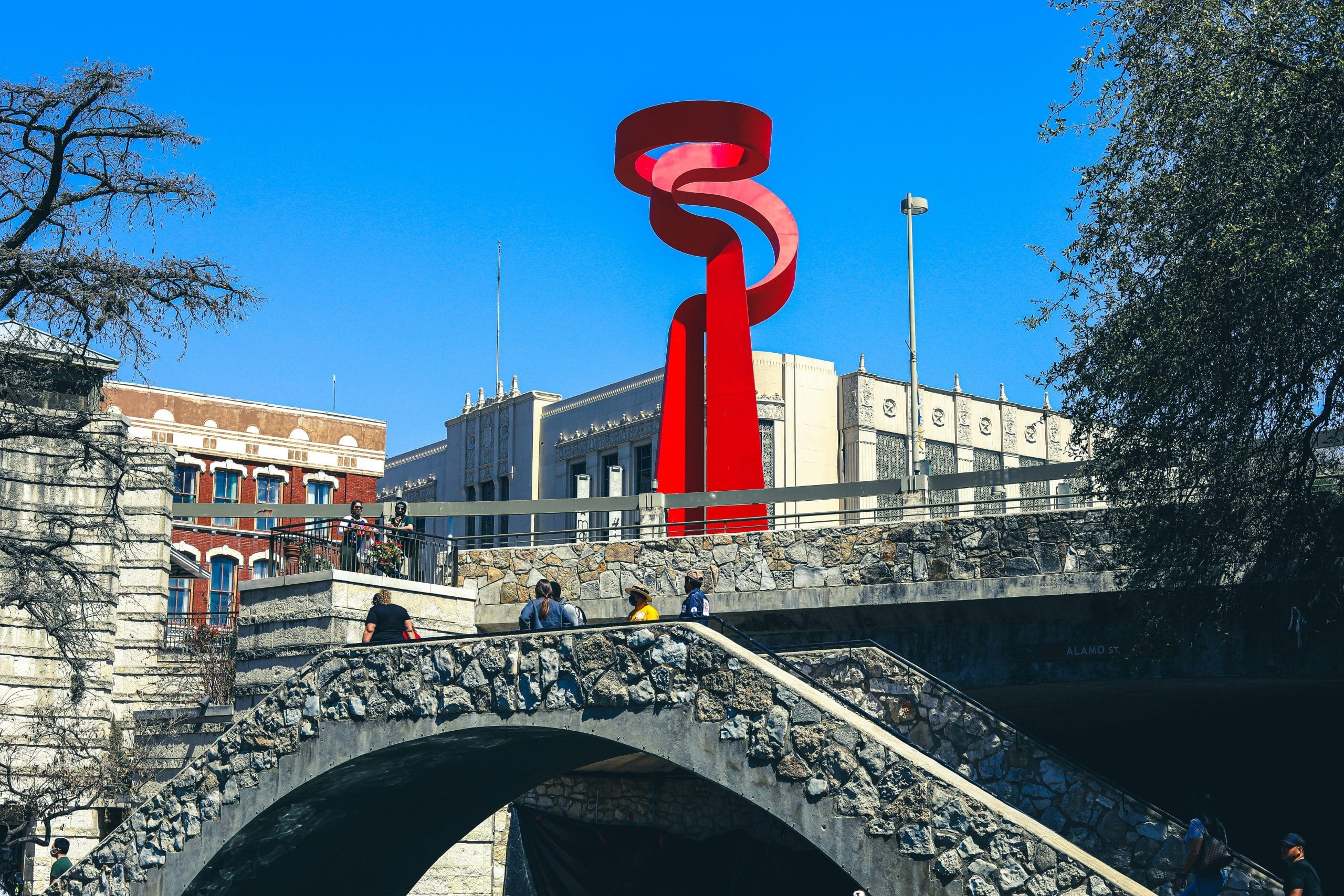 Red sculpture overlooking a stone bridge along the San Antonio River Walk